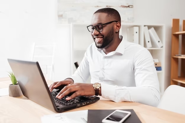 portrait-homme-affaires-afro-americain-souriant-chemise-blanche-lunettes-assis-travaillant-son-ordin